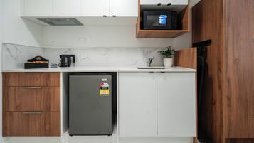 A compact kitchen with white cabinets, a built-in microwave, a refrigerator, and a coffee maker.