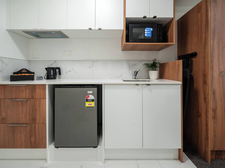 A compact kitchen with white cabinets, a built-in microwave, a refrigerator, and a coffee maker.