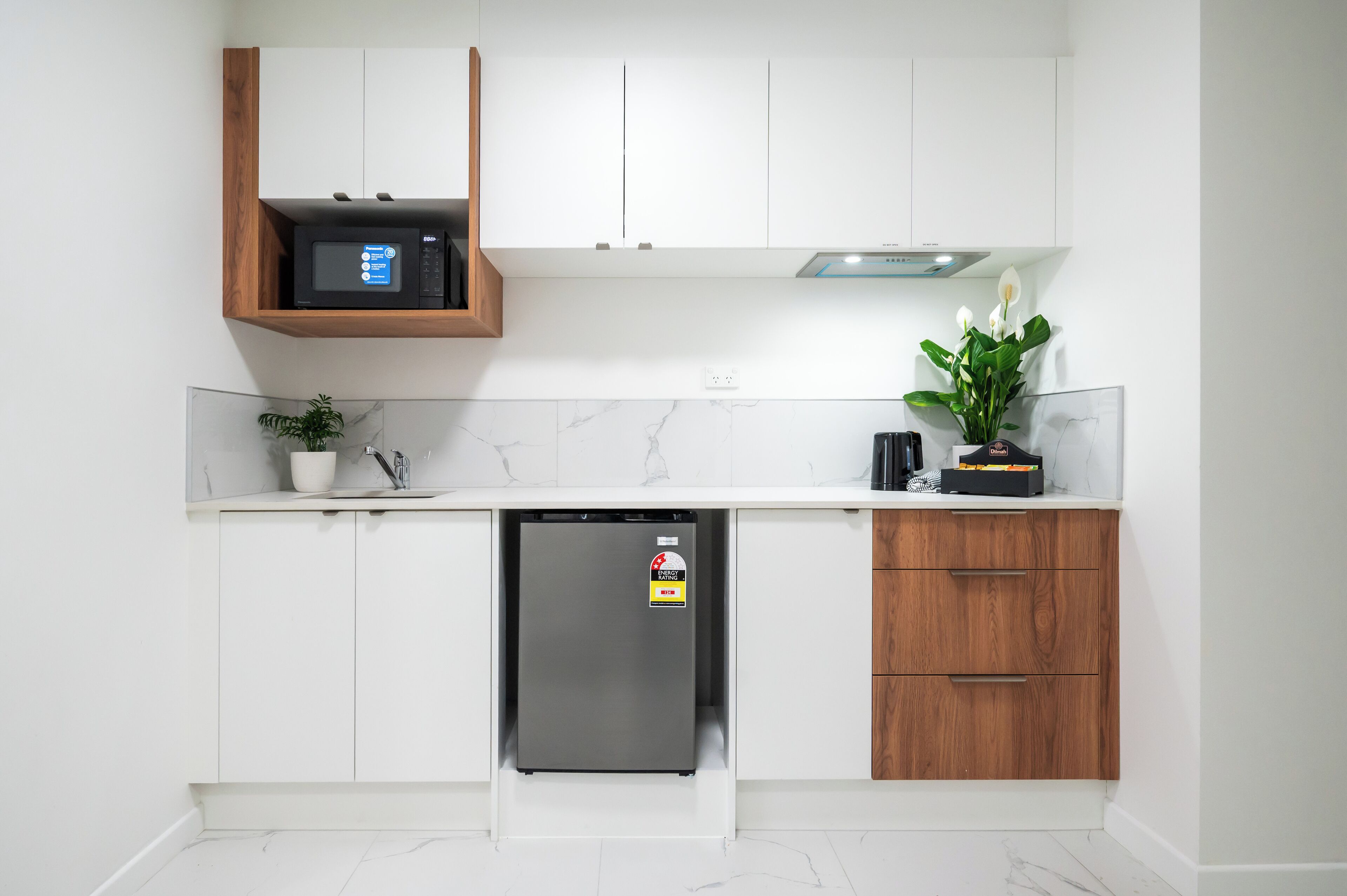 A compact kitchen with white cabinets, a built-in microwave, a stainless steel refrigerator, and a potted plant.