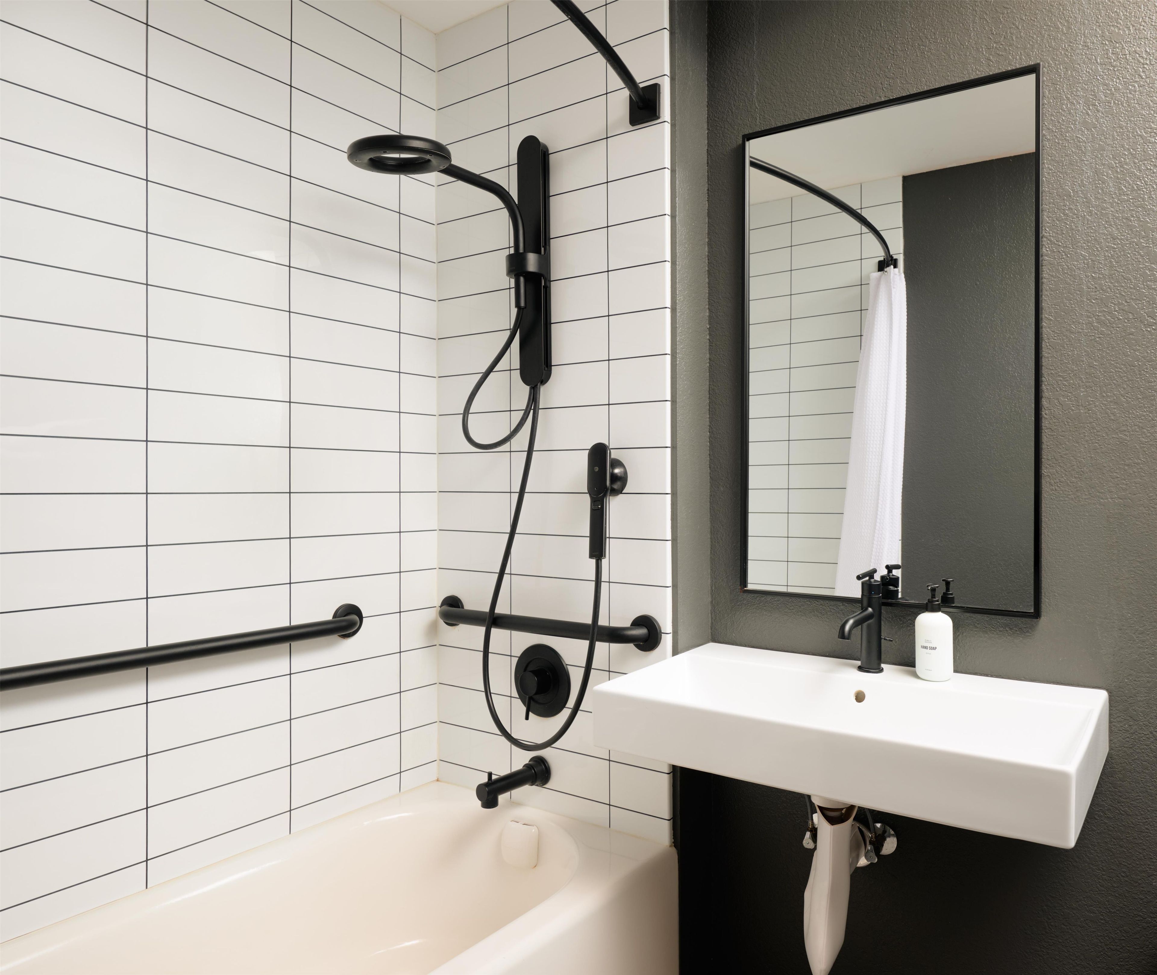 A modern bathroom with a white bathtub, black fixtures, a white sink, and a mirror.