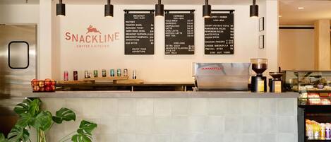 A snack bar with a menu board, a coffee machine, and a variety of beverages.