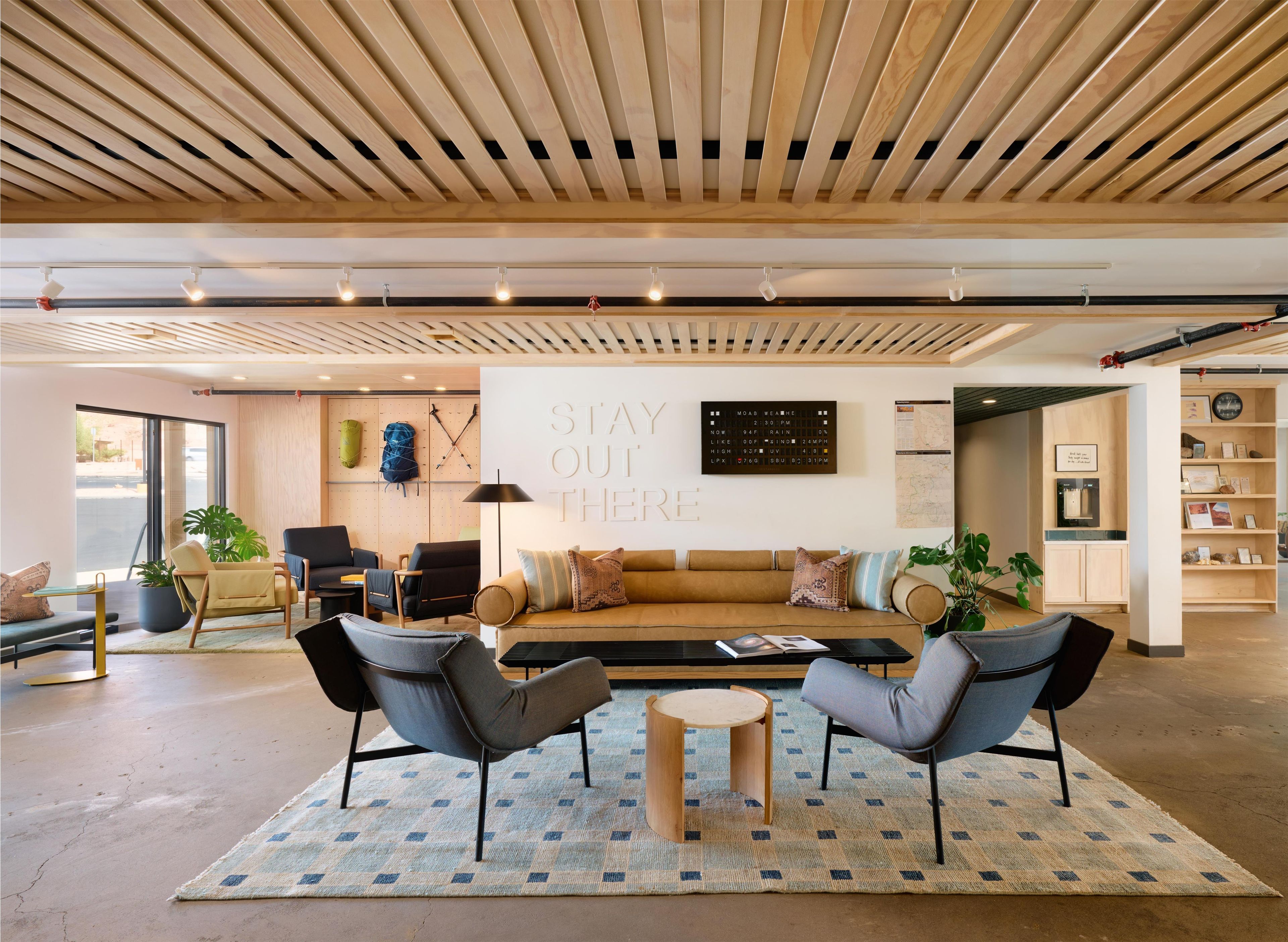 Un espace de détente moderne avec un plafond en bois, des sièges confortables, une grande horloge murale et une citation inspirante.
