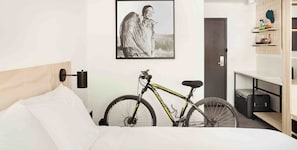 A hotel room with a bed, a bicycle, a framed picture on the wall, and a wardrobe with shelves. - Slackline Moab, Outset Collection by Hilton (Moab)
