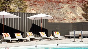 A pool area with lounge chairs and umbrellas, a hot tub, and a view of a red rock landscape.
