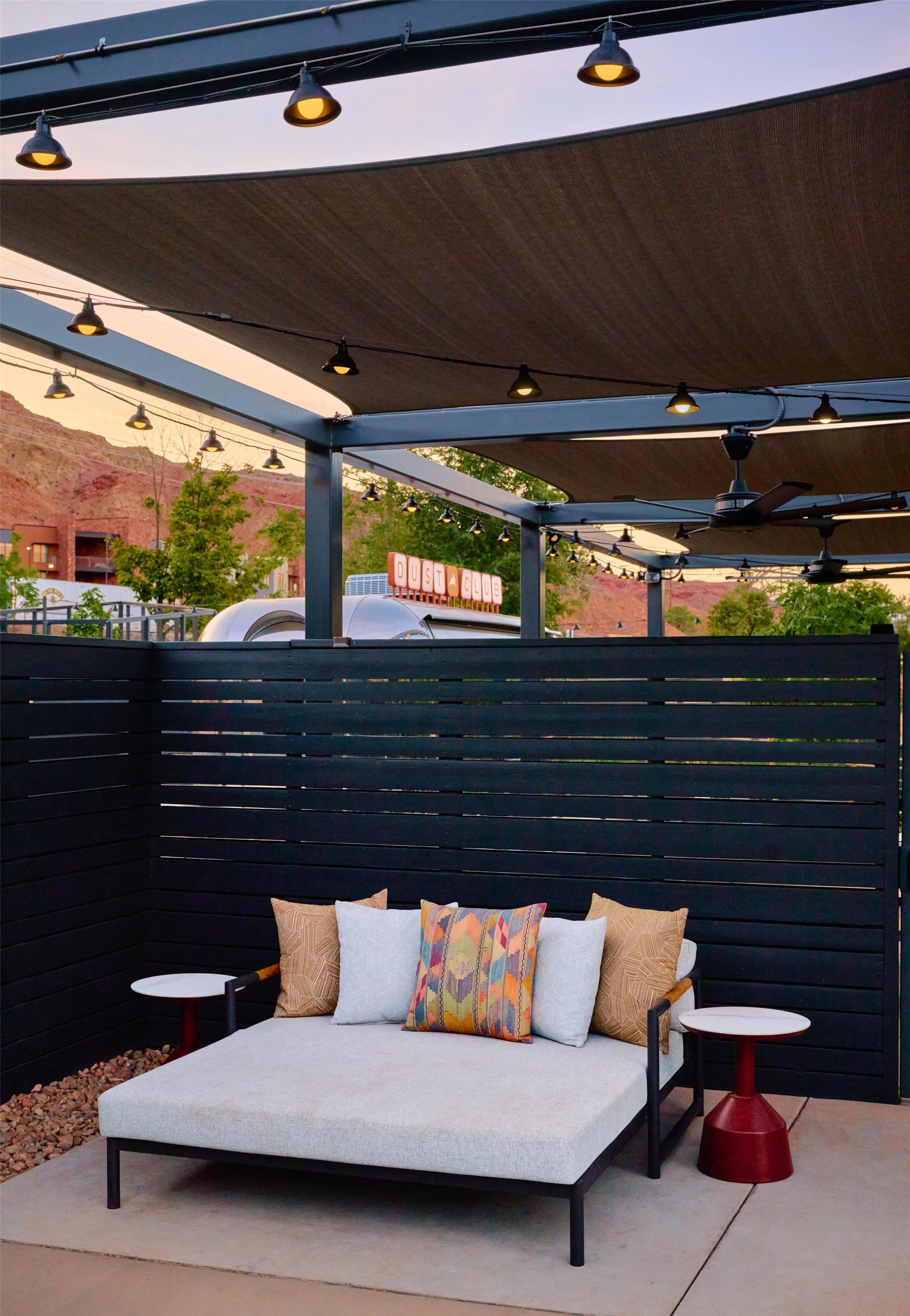 An outdoor seating area with a sofa and two small tables, a canopy overhead, and a sign reading 'DUST CLUB'.