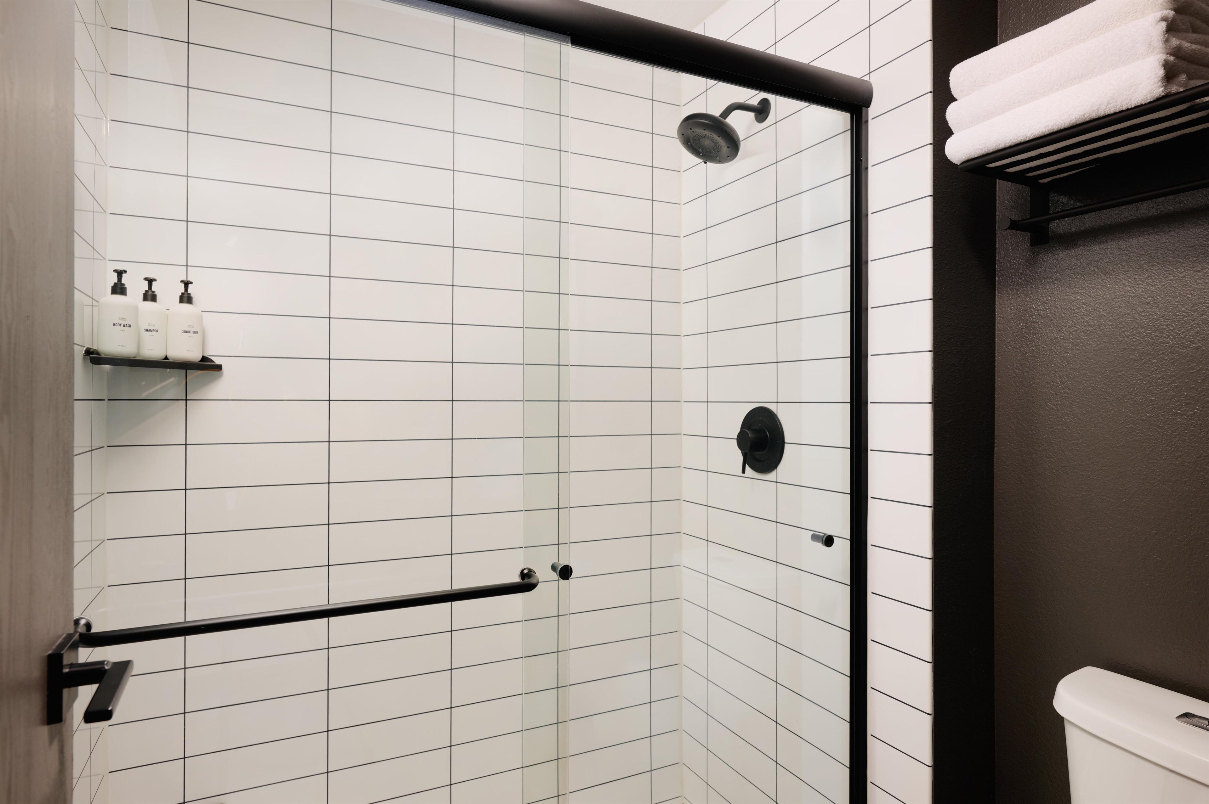 Een moderne badkamer met een douche, toilet en handdoekhouder.