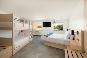 A room with bunk beds, a single bed, a flat-screen TV, and a window with a view of a desert landscape. - Slackline Moab, Outset Collection by Hilton (Moab)