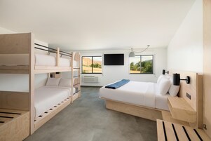 Una habitación con literas, una cama individual, un televisor de pantalla plana y una ventana con vista a un paisaje desértico.