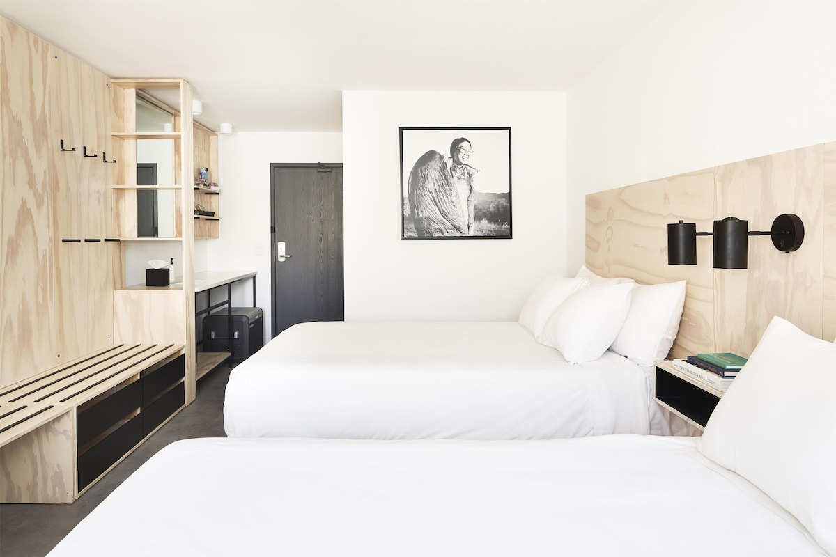 A modern hotel room with a bed, bedside tables, a wardrobe, and a framed picture on the wall.