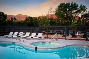 Un área de piscina con sillones, un jacuzzi y vistas a montañas.