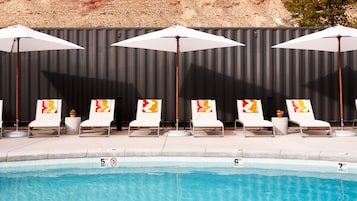 A poolside area with lounge chairs and umbrellas, a tiled pool edge, and a black wall in the background.