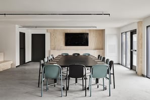A conference room with a long table, chairs, and a large screen on the wall.