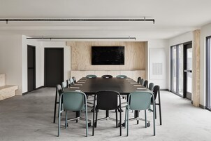 Un salón de conferencias con una larga mesa, sillas y una pantalla grande en la pared.