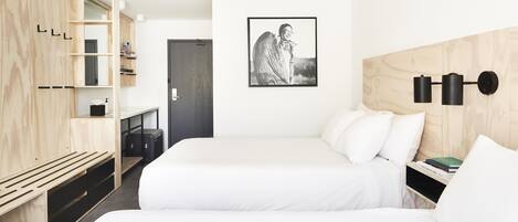 A minimalist hotel room with two beds, a wooden wardrobe, and a framed picture on the wall.