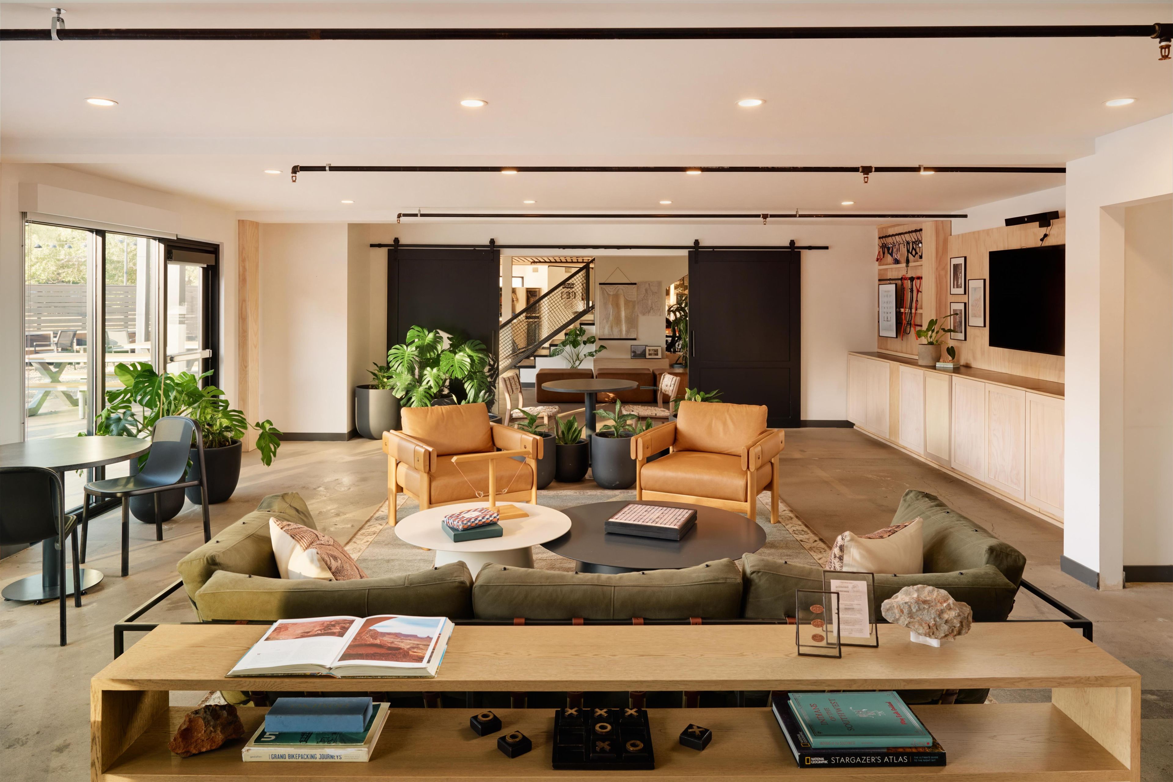 A spacious living area with a sofa, coffee table, and chairs, a dining table with books, and a kitchen area with a TV.