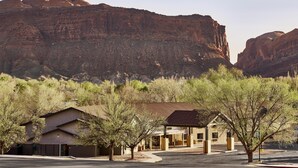 A building with a flat roof and a simple, modern design, surrounded by trees and set against a backdrop of red rock formations. - Slackline Moab, Outset Collection by Hilton (Moab)