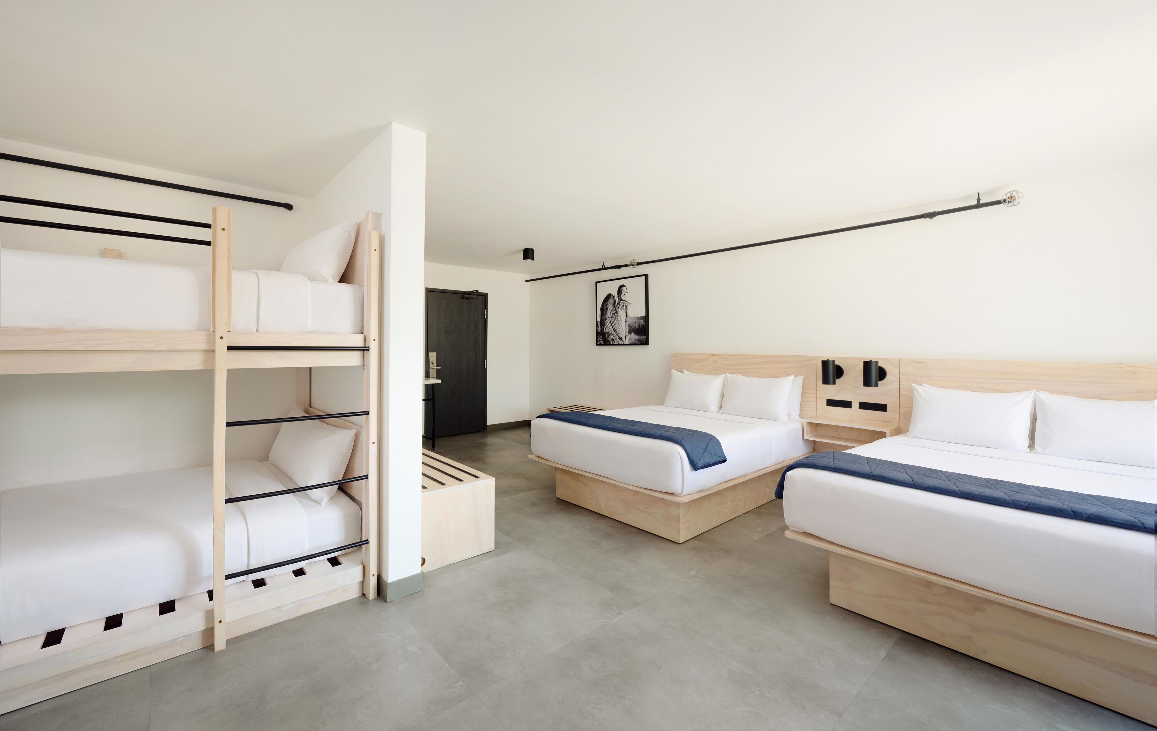 A hotel room with bunk beds, a single bed, and a headboard with storage compartments.