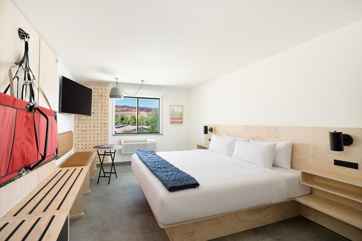 A modern hotel room with a bed, desk, chair, and a TV mounted on the wall.
