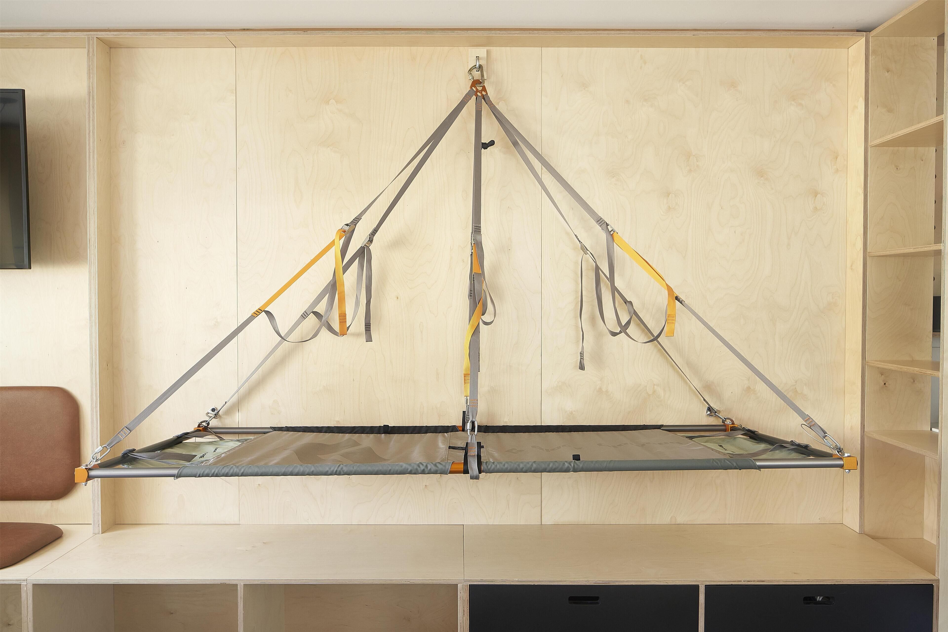 A room with a suspended hammock bed, wooden walls, and built-in shelving.