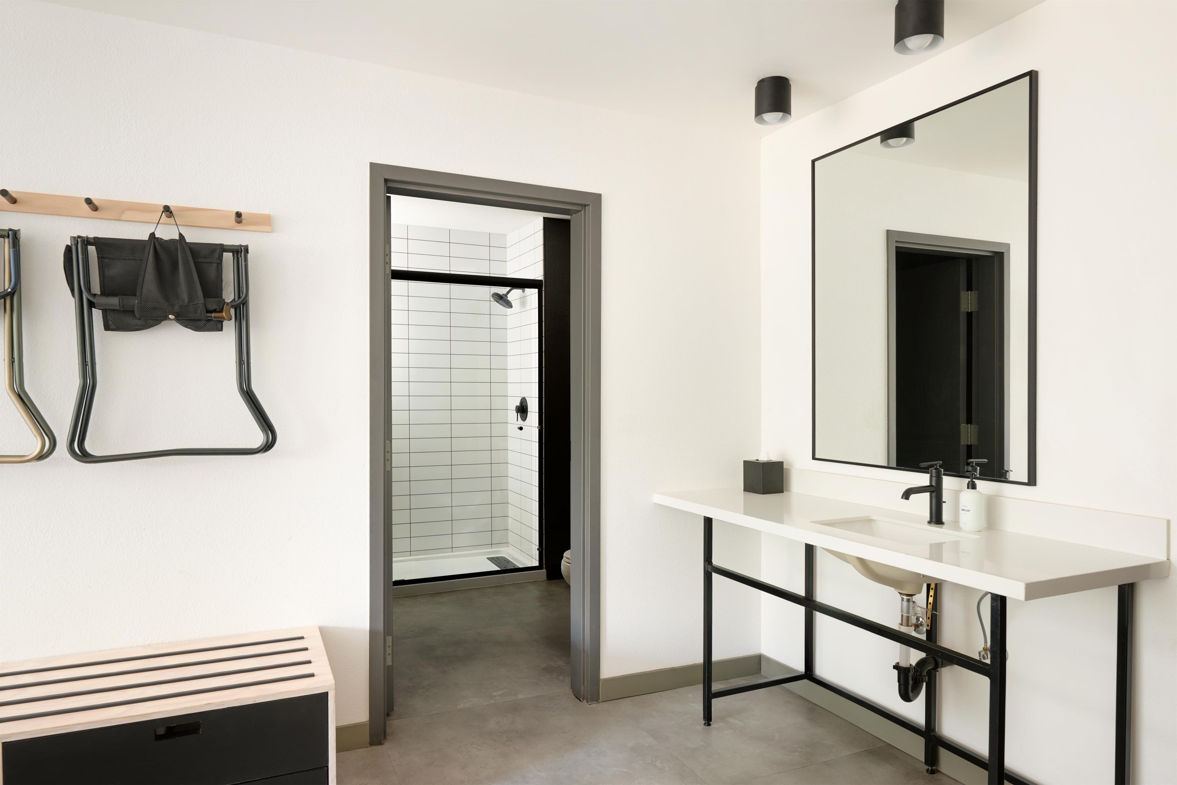 A modern bathroom with a white sink, black faucet, and a large mirror. There is a shower area visible through an open door.