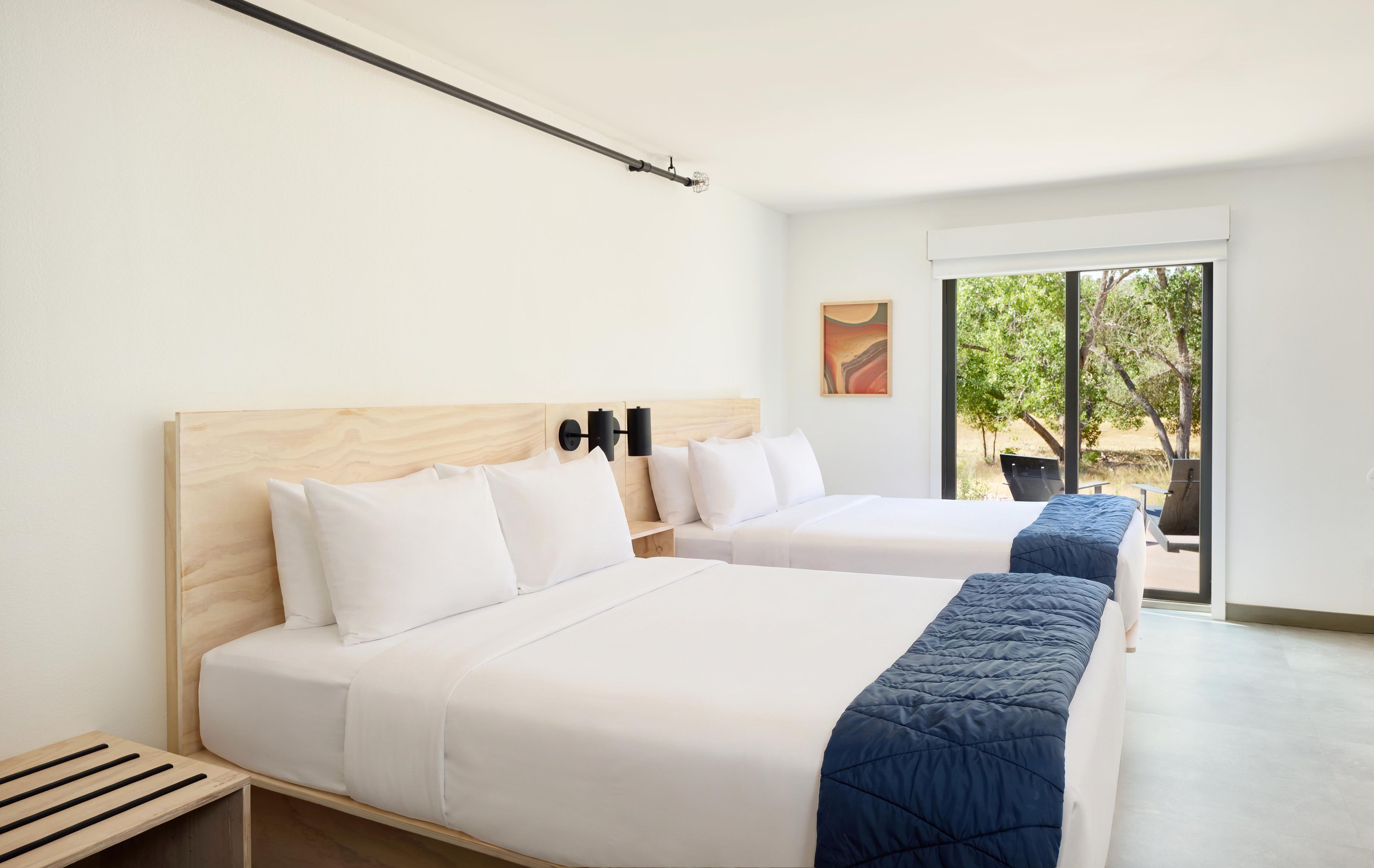 A hotel room with two beds, a large window, and a view of the outdoors.