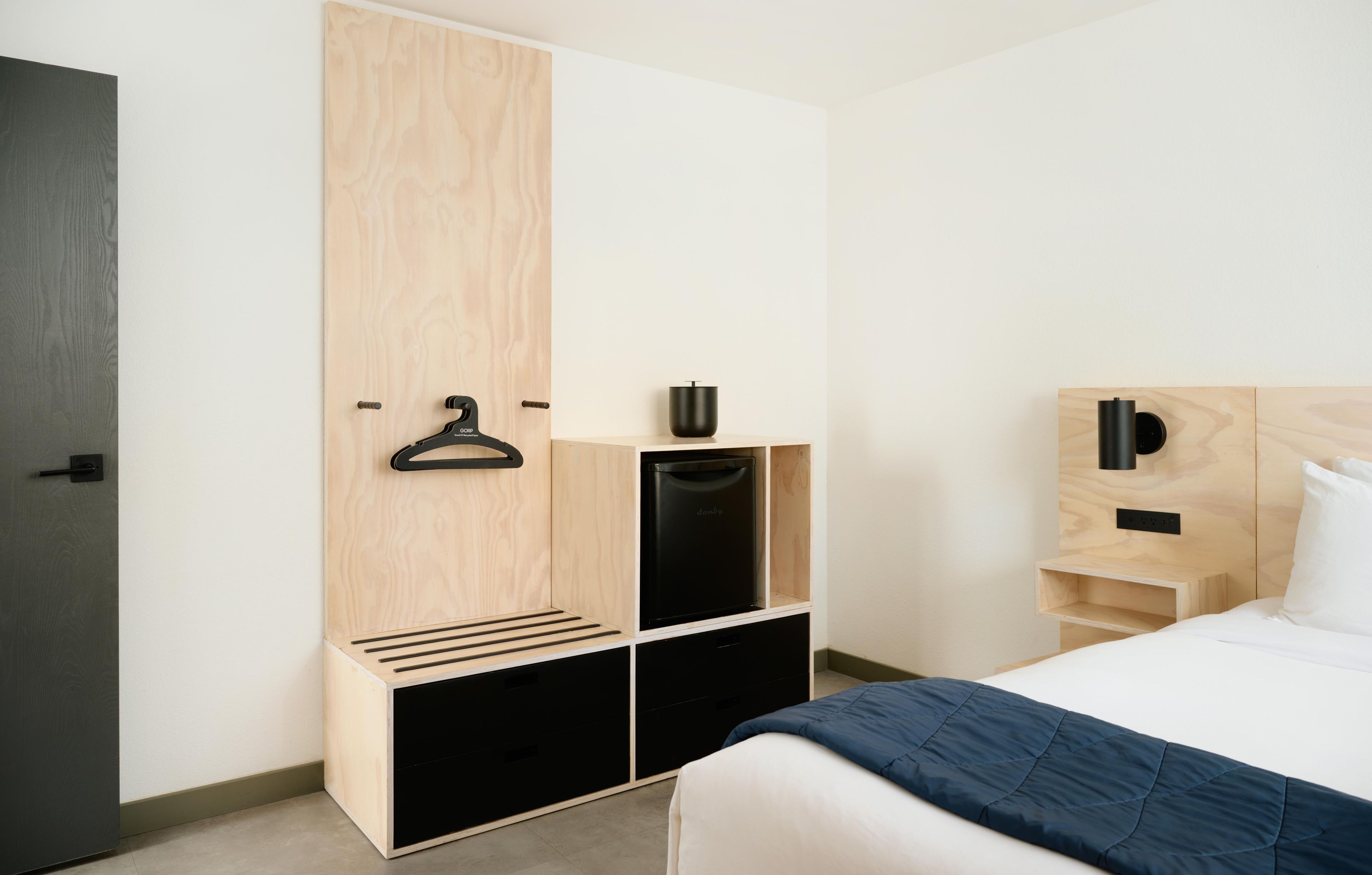 Een moderne slaapkamer met een bed, een garderobe met opbergrek, een zwart apparaat en een nachtkastje met een lamp.