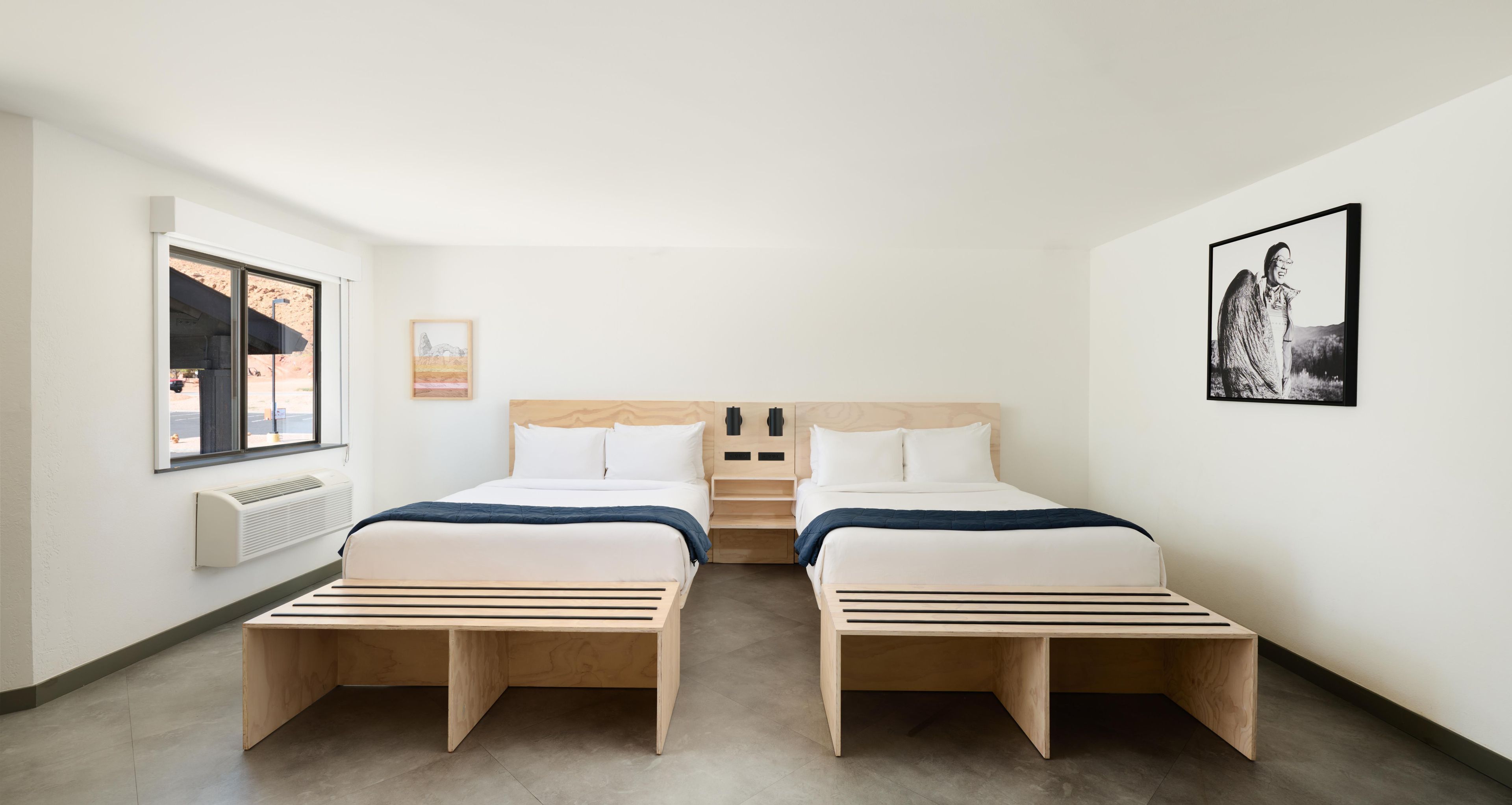 Habitación de hotel con dos camas, una ventana, un radiador y obras de arte en las paredes.