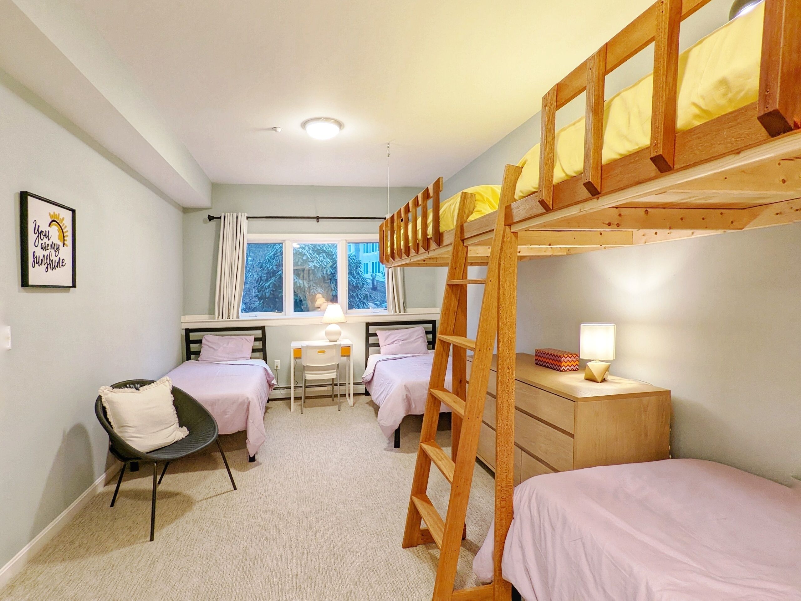 Une chambre de dortoir avec des lits superposés, un bureau, une chaise et une échelle.