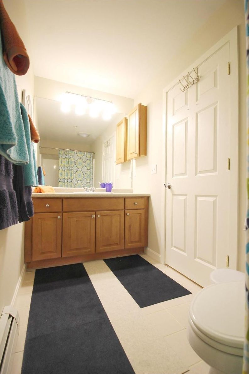 A bathroom with wooden cabinets, a white toilet, and a black and white rug.