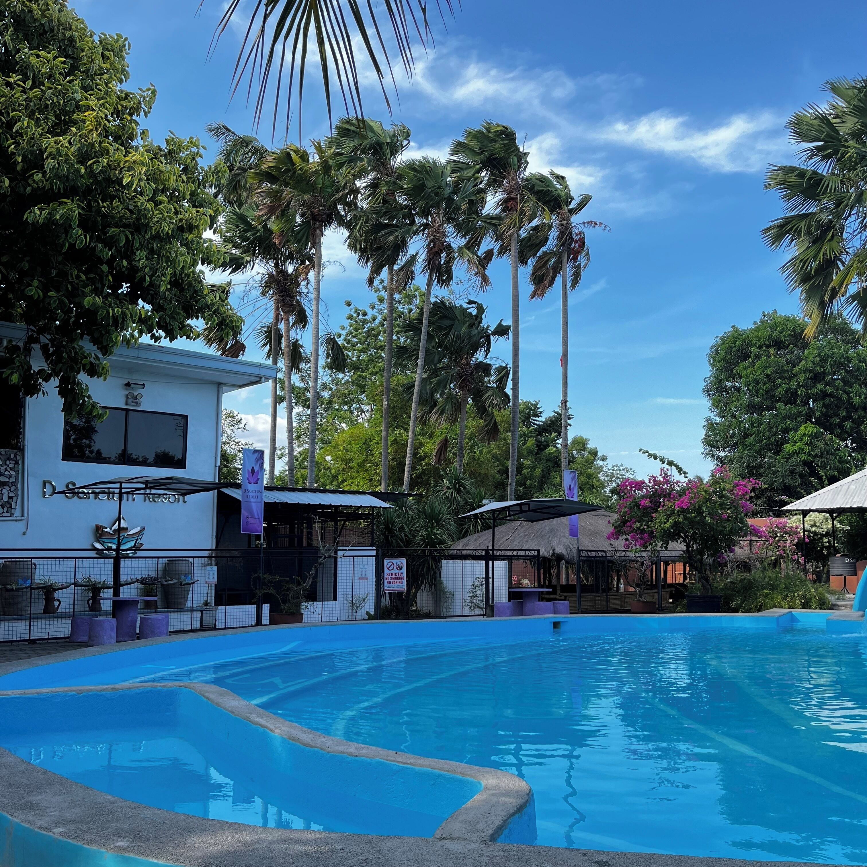 Um resort com piscina, palmeiras e um edifício com uma placa.