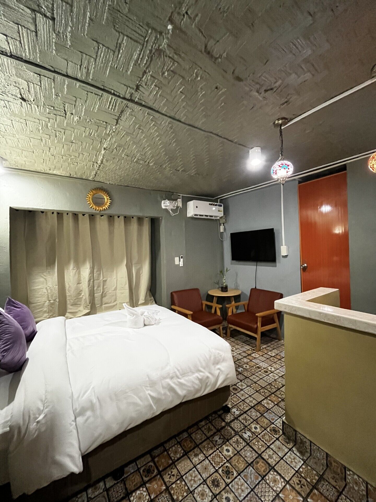 Habitación de hotel con cama, escritorio, silla, televisor y techo con textura.