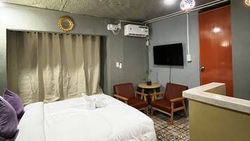 Habitación de hotel con cama, escritorio, silla, televisor y techo con textura.