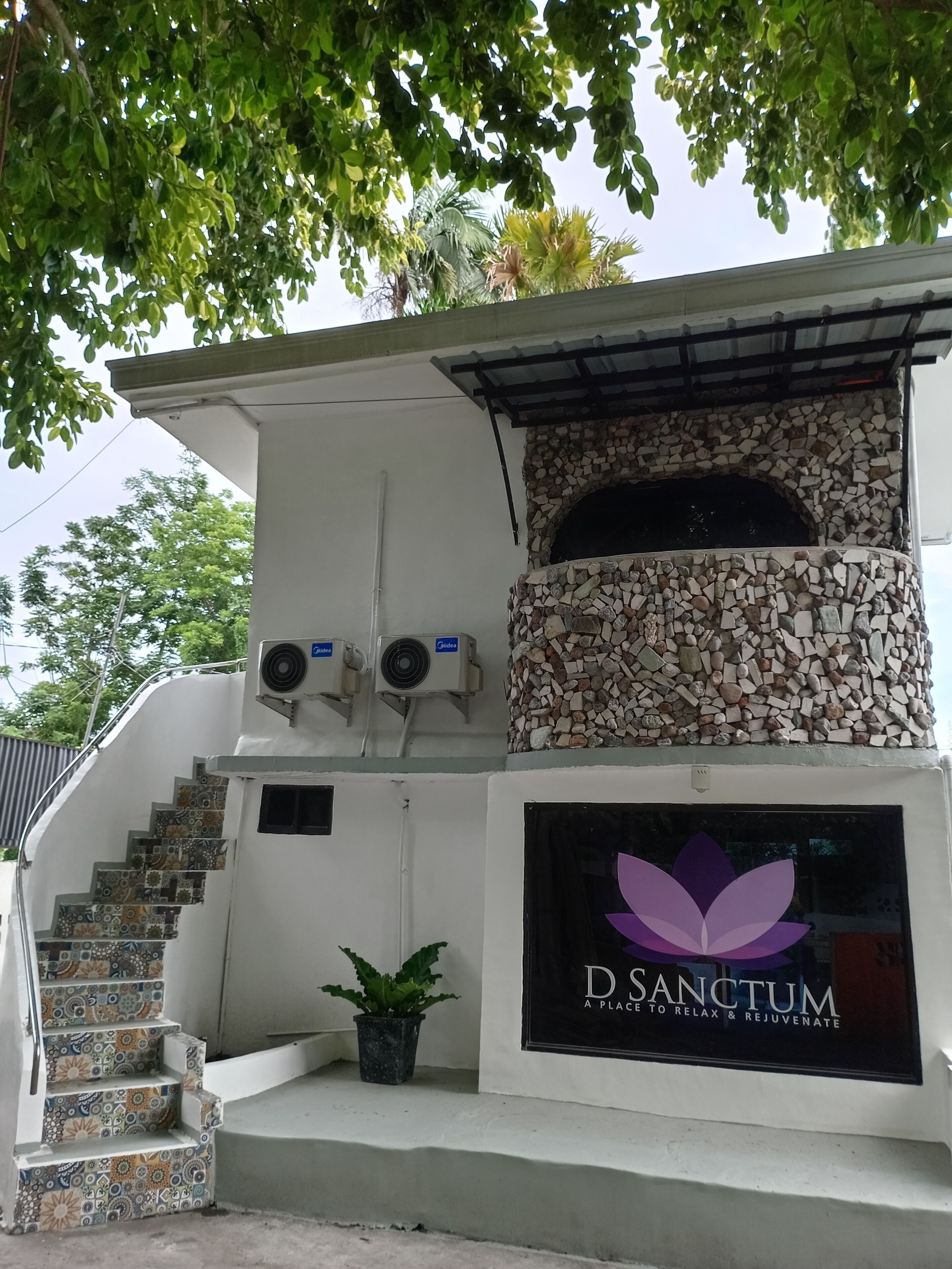 Un edificio con fachada de piedra, un logo con una flor de loto y una escalera con baldosas estampadas.