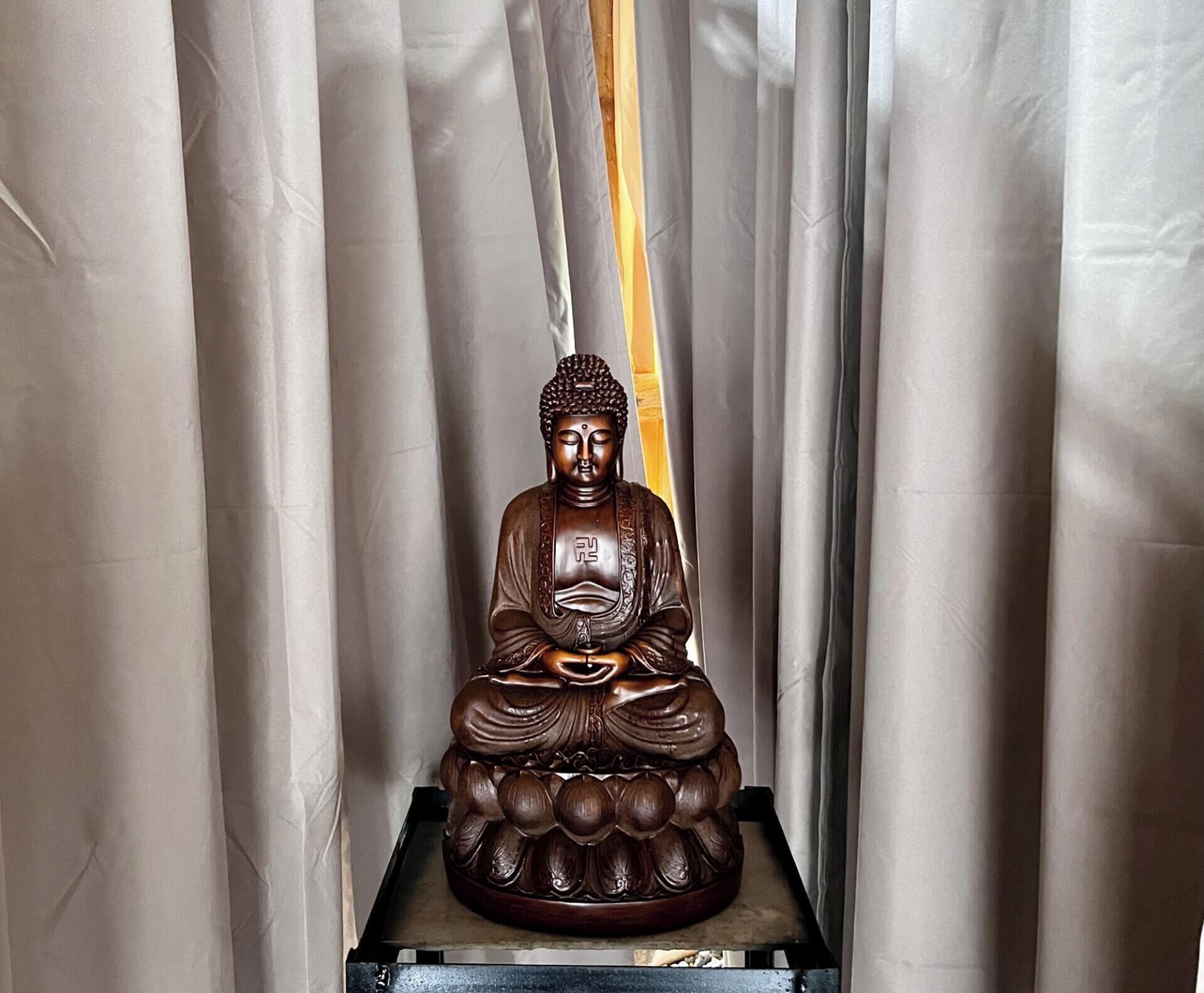Estatua sentada de una figura en posición meditativa, sobre un pedestal.