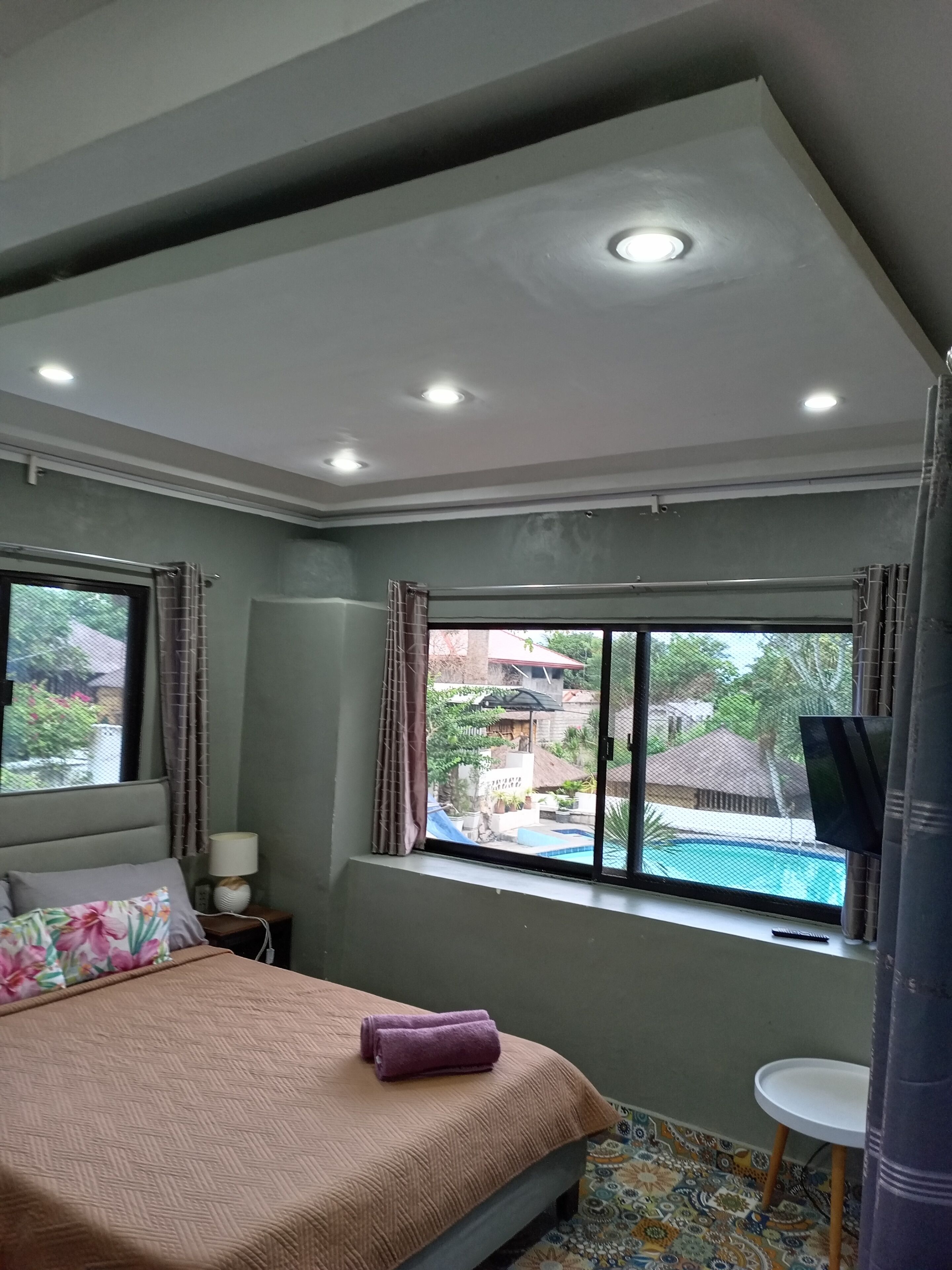 A bedroom with a bed, a window, a TV, and a small table.