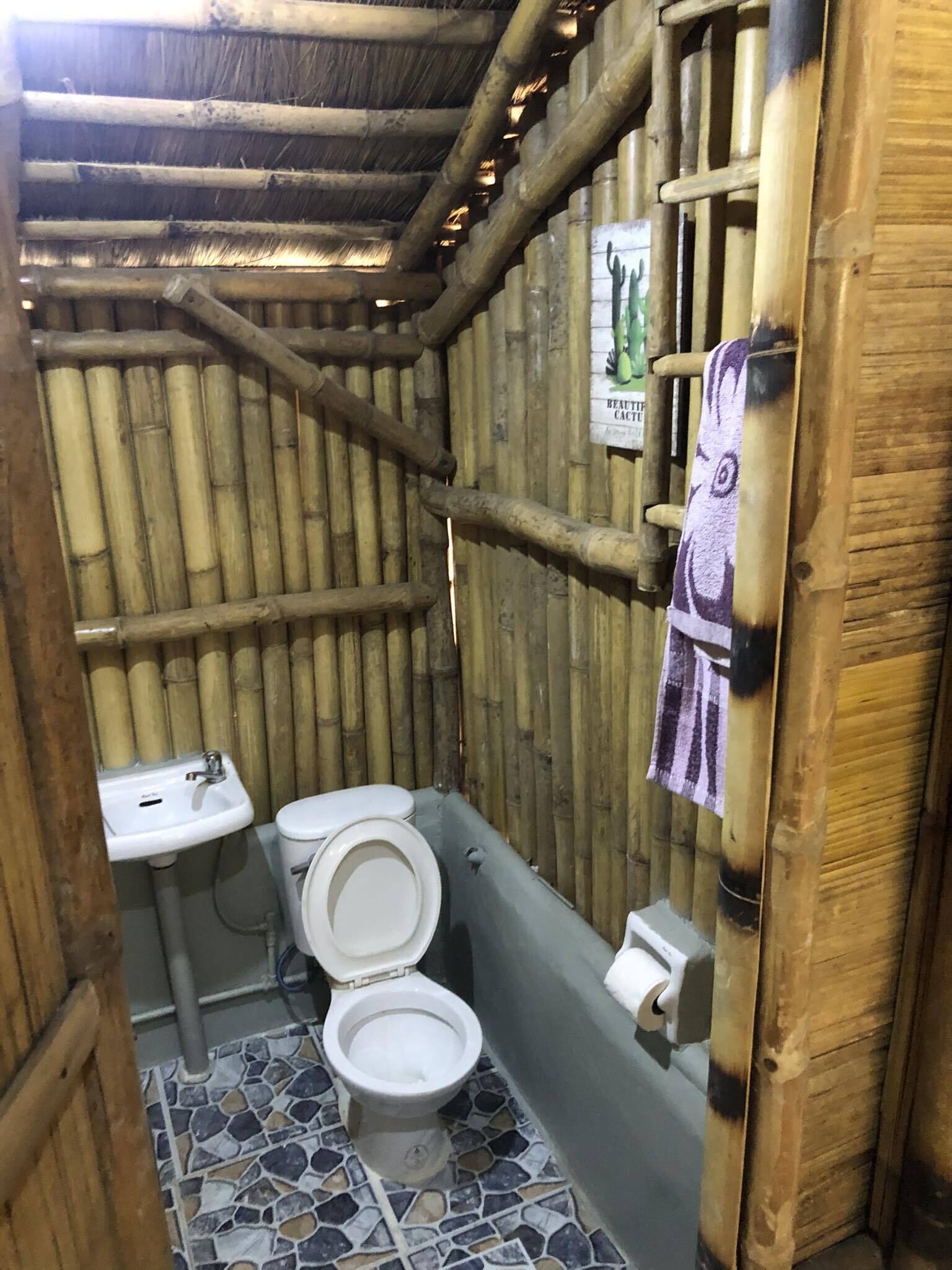 Ein kleines Badezimmer mit Toilette, Waschbecken und Duschbereich, ausgestattet mit Bambuswänden und Fliesenboden.