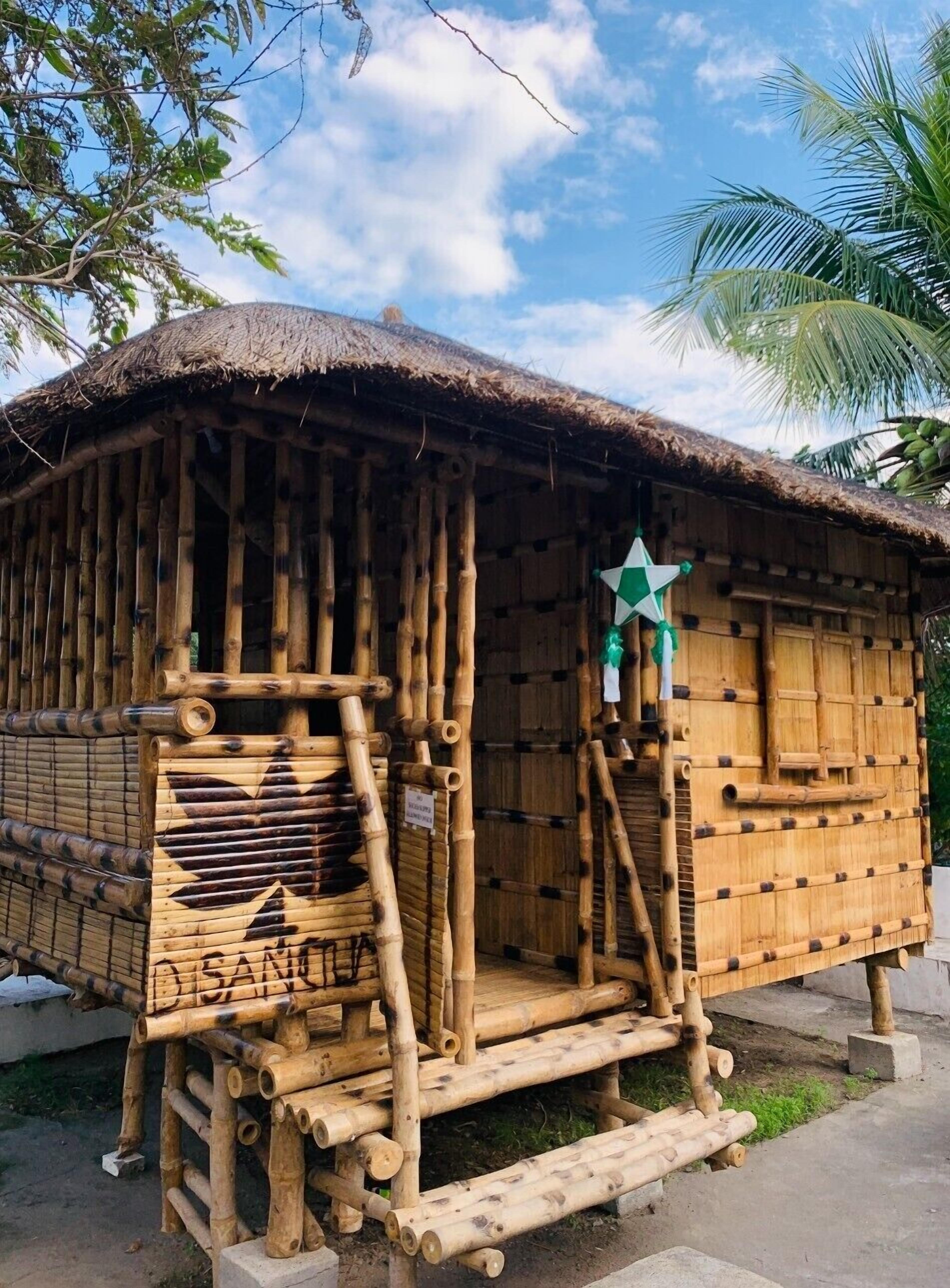 Una estructura tradicional de bambú con techo de paja, una decoración de estrella y una escalera que lleva a la entrada.