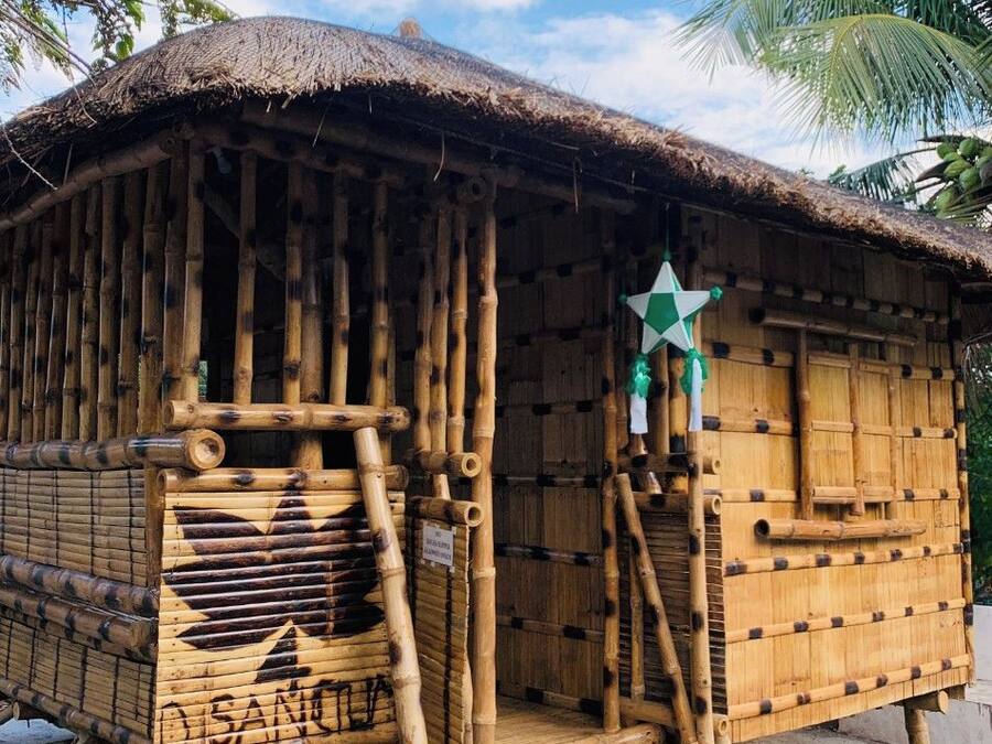 A traditional bamboo structure with a thatched roof, a star decoration, and a staircase leading to the entrance.
