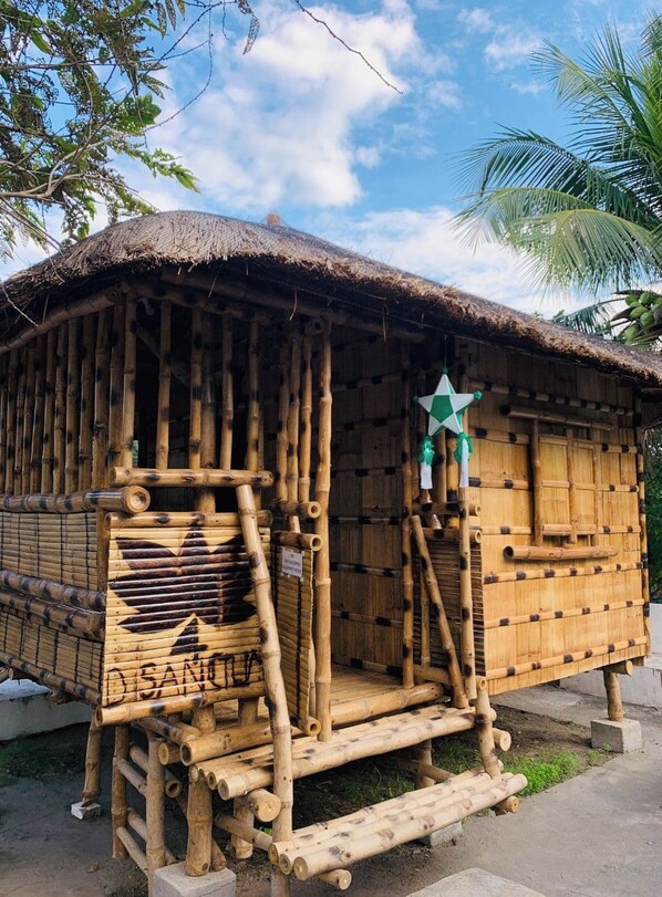 Una estructura tradicional de bambú con techo de paja, una decoración de estrella y una escalera que lleva a la entrada.