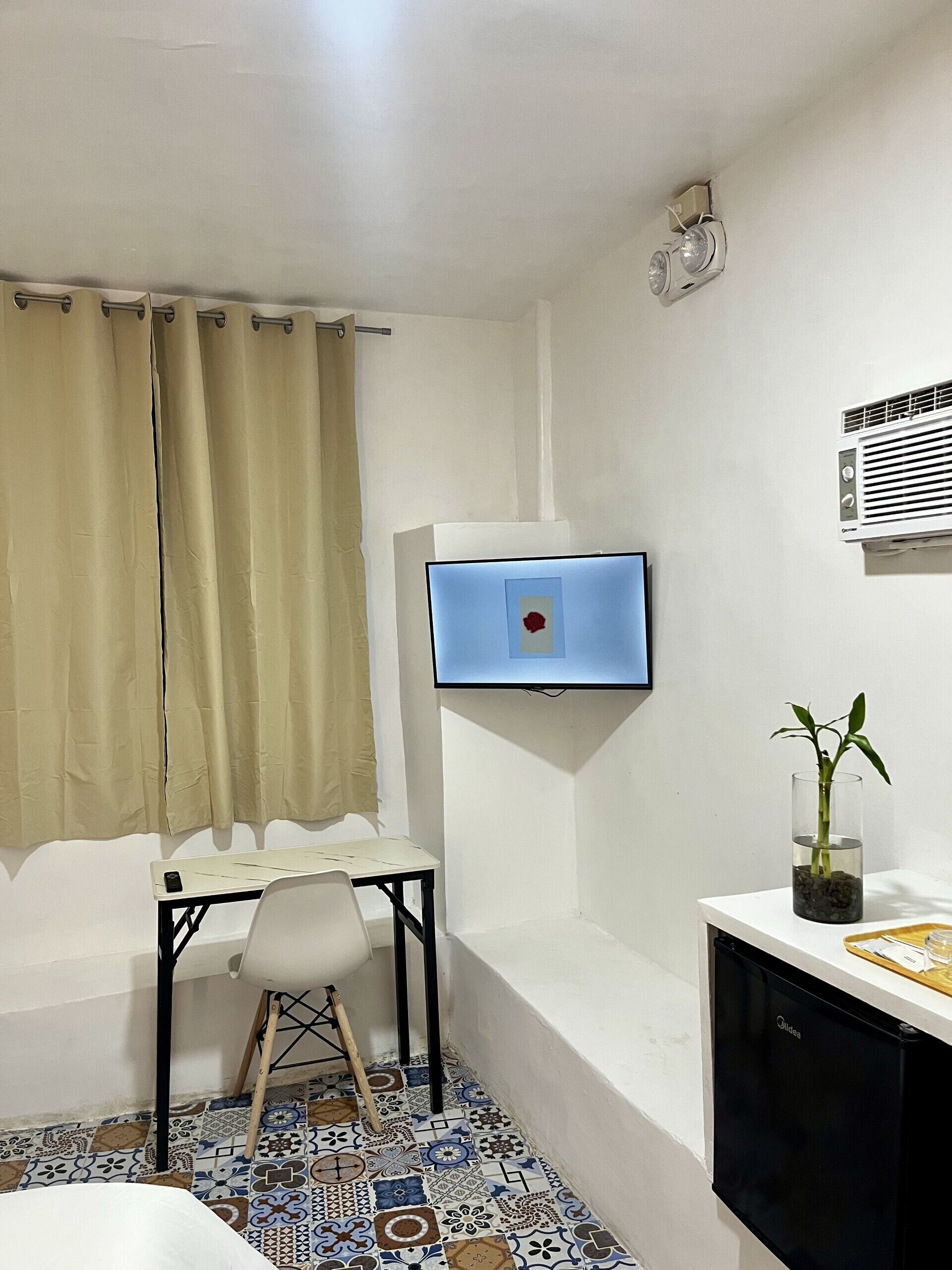 Quarto pequeno com escrivaninha, cadeira, televisão e um vaso de planta.