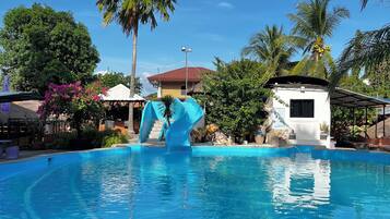 Ein Swimmingpool mit blauer Rutsche, umgeben von Palmen und einem kleinen weißen Gebäude.