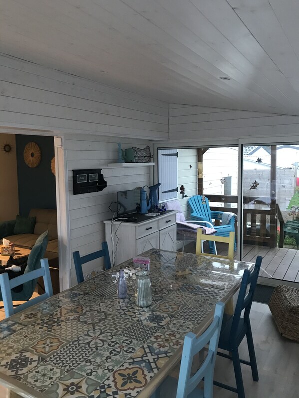 A dining area with a patterned table and blue chairs, a kitchen with white cabinets, and a view of the outside through a glass door.