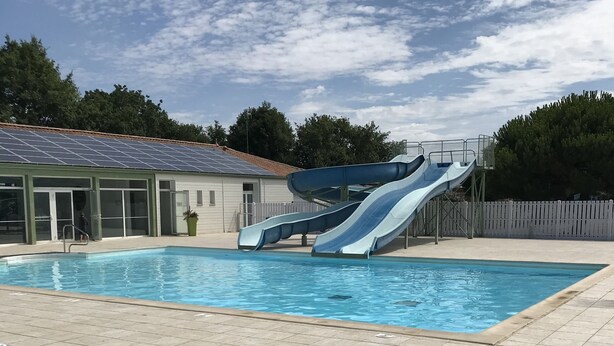 Ein Schwimmbecken mit zwei Wasserrutschen, überdachtem Bereich und umzäunter Fläche.