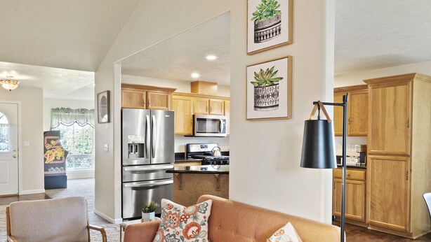 A spacious living room with a large sofa, a coffee table, and a kitchen in the background. - Charming white picket fenced home in quiet area (Medford)