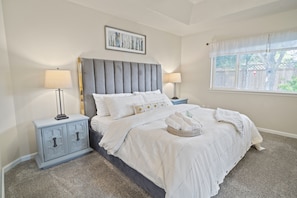 Une chambre à coucher avec un grand lit, deux tables de chevet, une fenêtre donnant sur un beau paysage et un luminaire au plafond.