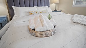A neatly made bed with a white comforter, a decorative pillow, and a towel basket. - Charming white picket fenced home in quiet area (Medford)