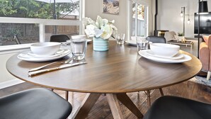 A dining area with a round wooden table, two chairs, white dinnerware, and a vase with white flowers. - Charming white picket fenced home in quiet area (Medford)