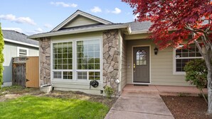 A single-story house with a stone facade, large windows, and a front door. - Charming white picket fenced home in quiet area (Medford)