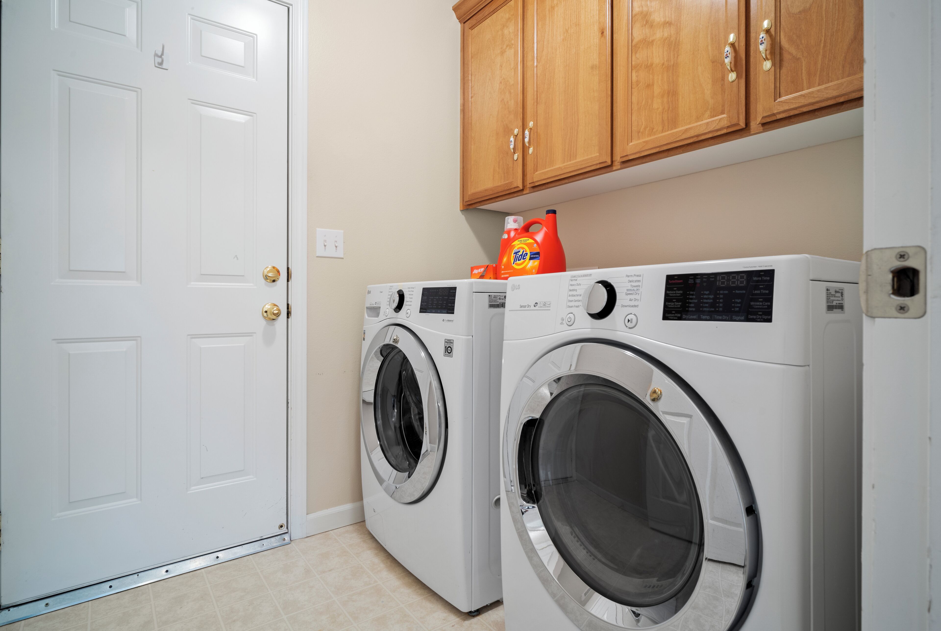 A laundry room with two front-loading washing machines, wooden cabinets above, and a white door.