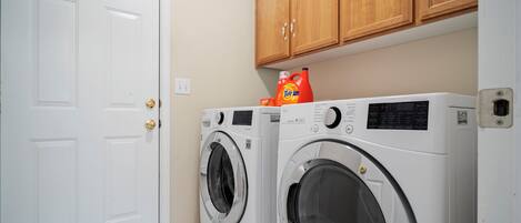 A laundry room with two front-loading washing machines, wooden cabinets above, and a white door.